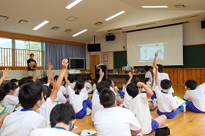 スクリーンのある教室内で生徒たちが集まっている写真