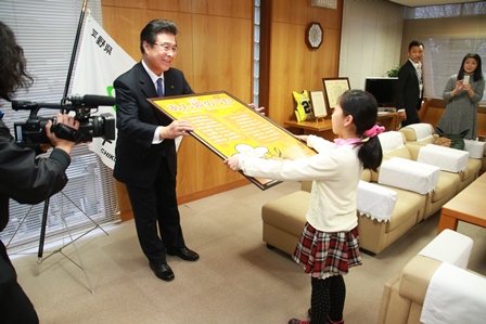 大きなパネルを両手で持ち、市長に手渡す大久保さんの写真
