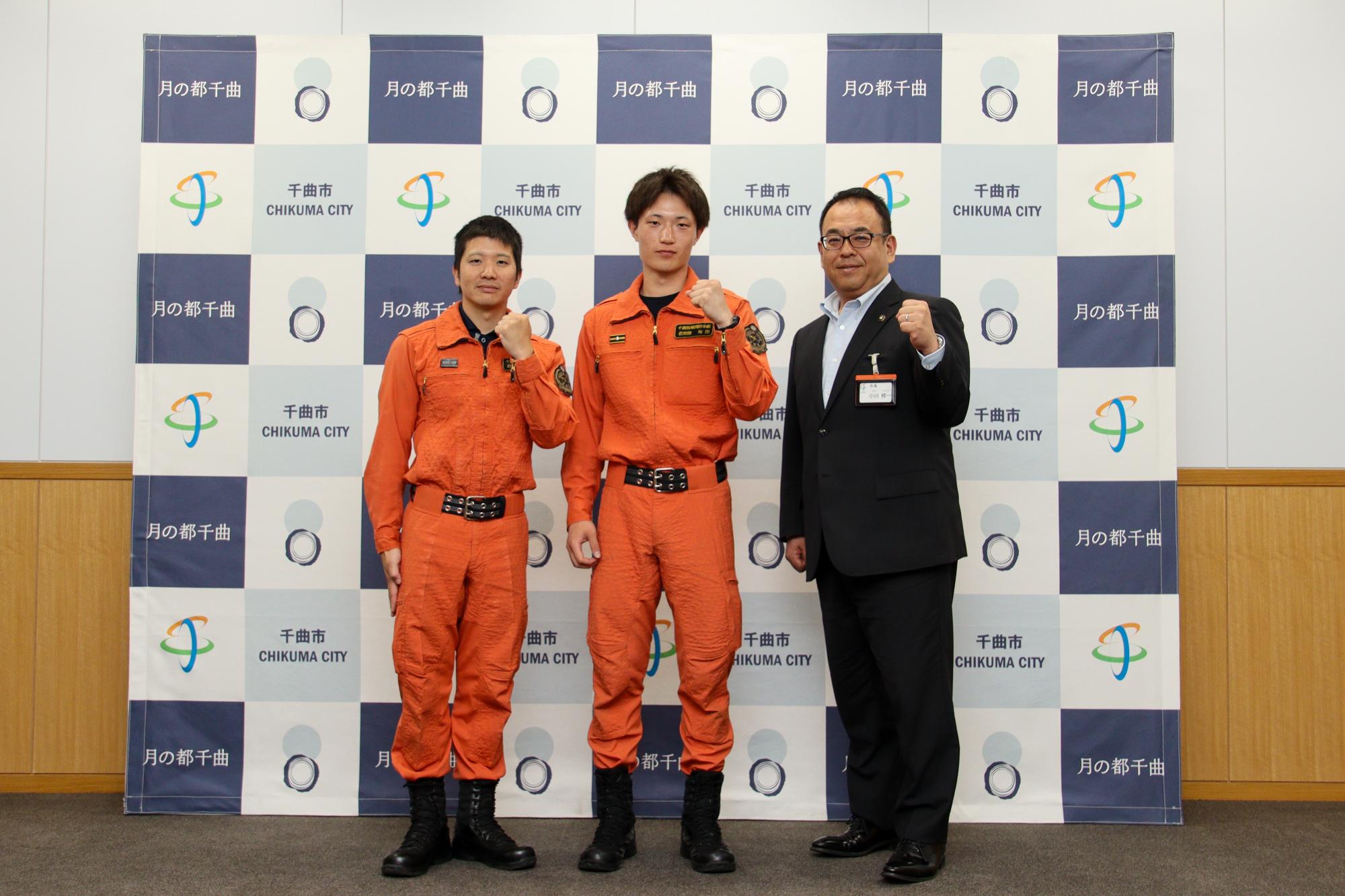 ガッツポーズをする、救助隊員2名（左から、丑丸隊員、梅田隊員）と小川市長（一番右）