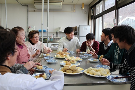 出来上がったおやきを美味しそうに食べている学生と稲荷山蔵の会のみなさんの写真