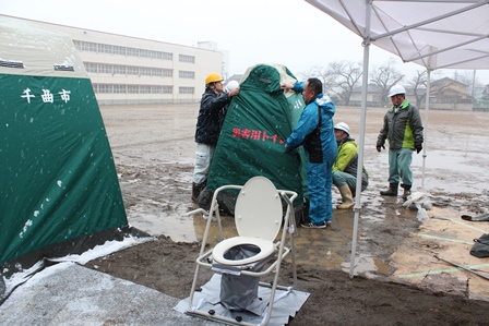 男性スタッフたちが災害用トイレを組み立てている写真