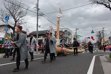 道路を移動する御柱が立った木製の舟と、共に歩く参加者達の写真