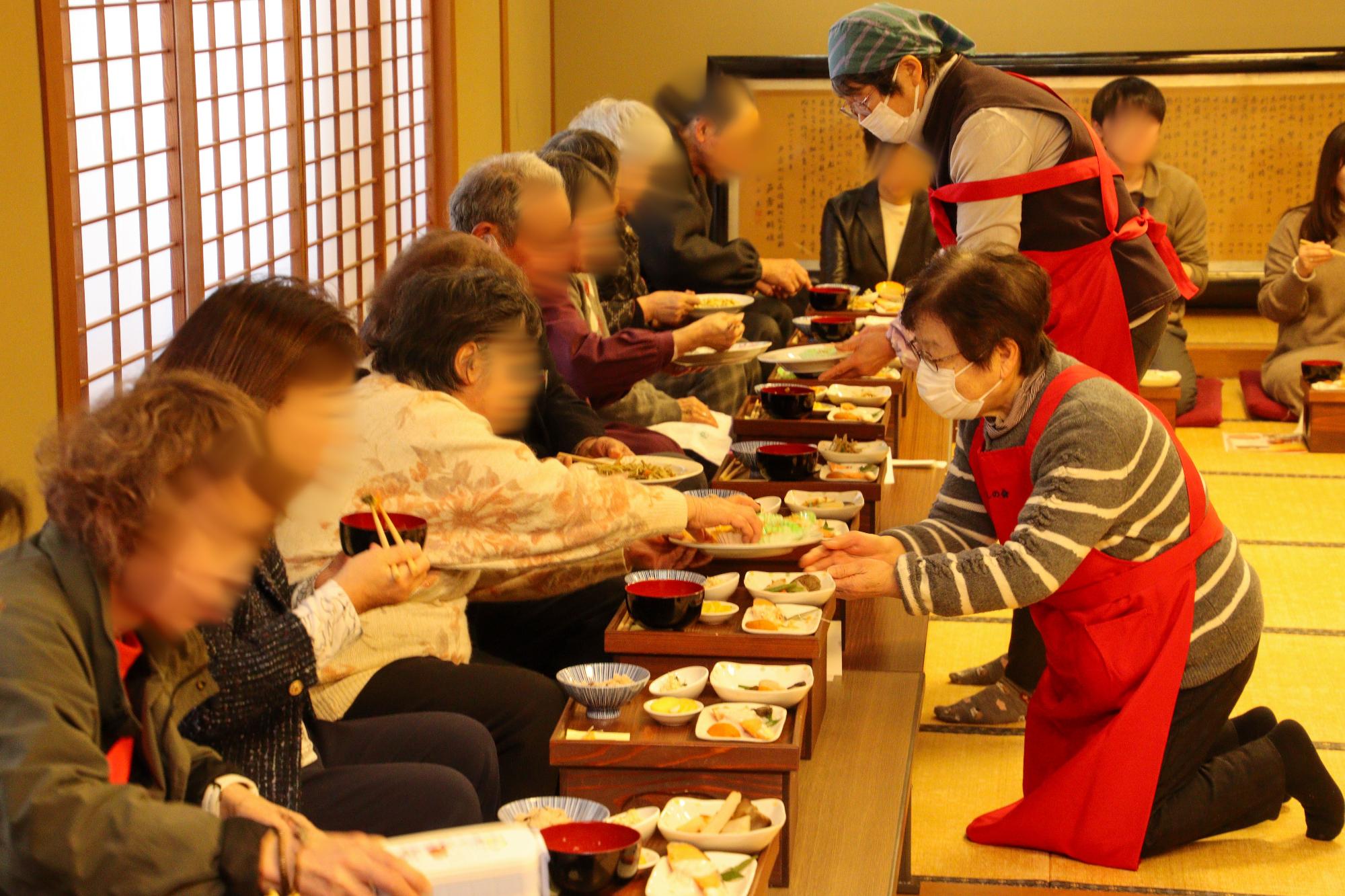 箱膳体験の様子。参加者に大皿の料理を配っているかけはしの会会員