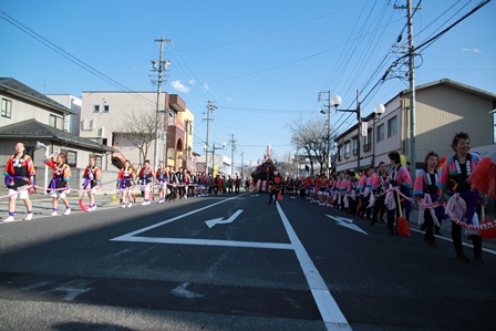 紅白の縄を持ち、道路の両側を列になって歩く法被姿の参加者達の写真