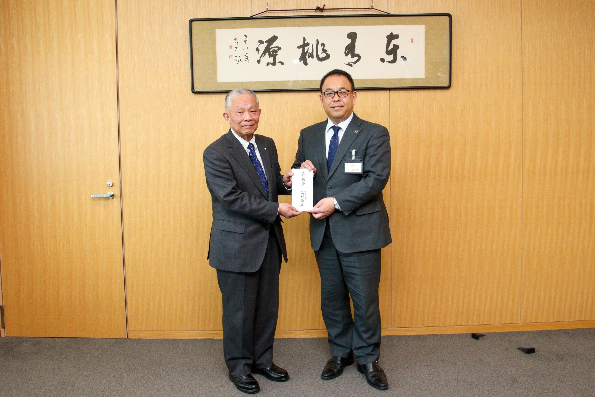 小川市長と高村代表取締役が義援金を持っている写真。右に小川市長、左に高村代表取締役。