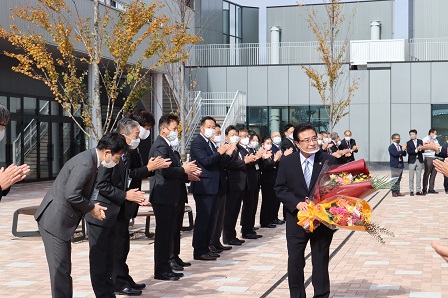 花束を受け取り拍手喝采で見送られる岡田市長の写真