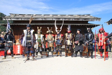 城跡前で鎧兜を着た9名の男性が記念撮影する写真
