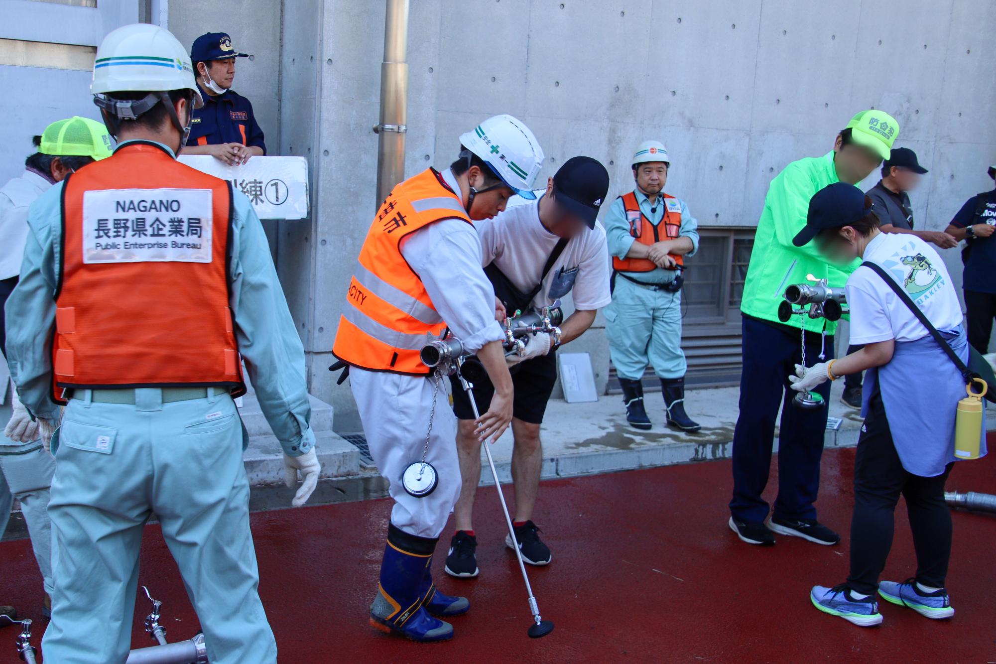 給水訓練で地下式消火栓を使用し、応急給水場所を設置している市職員と市民の様子