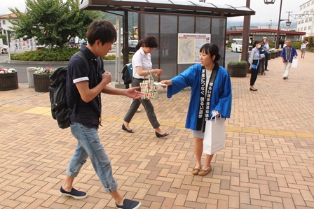 青色の半被を着た女性が駅前でティッシュを配っている写真