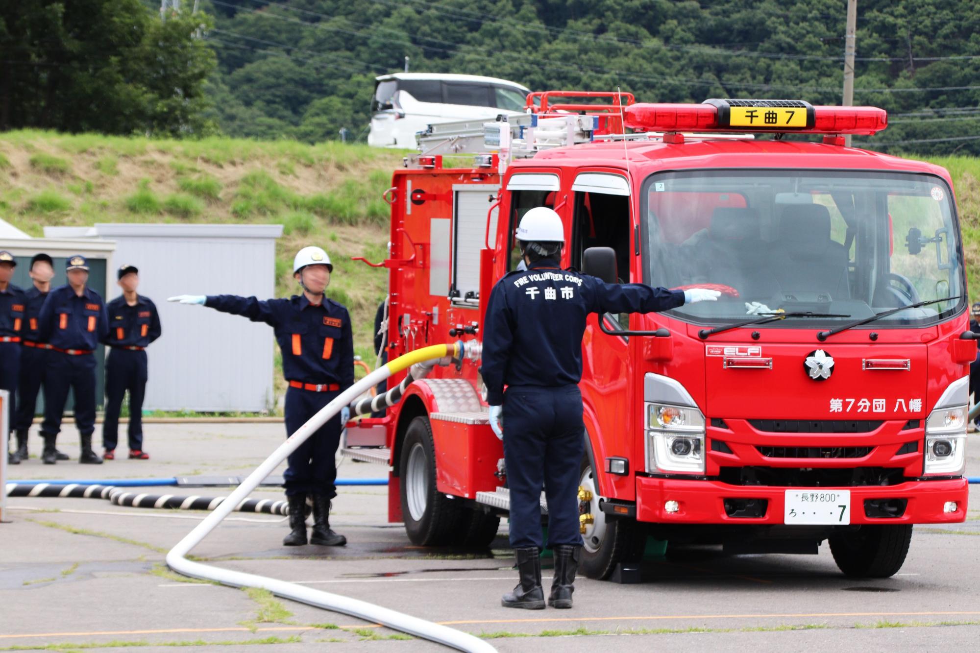 ポンプ車操法で、放水止めの合図をする3番員と、それに応答する4番員の様子