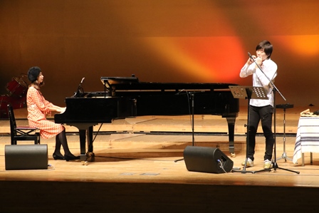 ステージ上でピアノの演奏をする女性とオカリナなどを吹く男性の写真