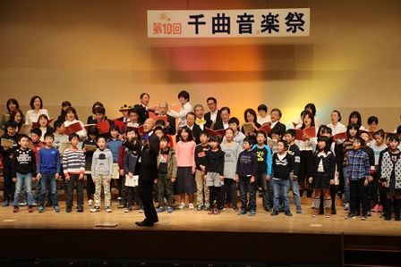 ステージで指揮をする男性と合唱をする小学生の写真