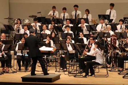 ステージで演奏する指揮者と吹奏楽団の写真