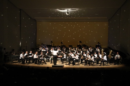 天井にミラーボールが回るステージで演奏する吹奏楽団の写真