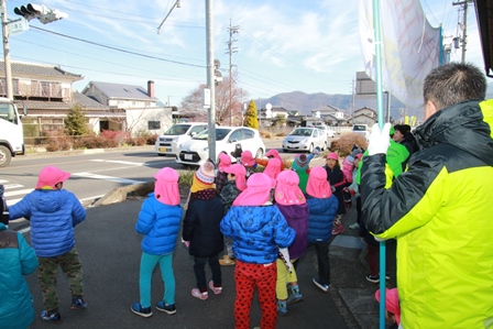 帽子を被った園児たちが列になって車道に向かい啓発活動をしている様子の写真