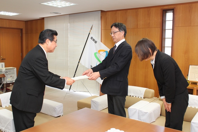 スーツ姿の男性と女性が市長に書類を手渡している写真