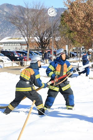 雪上で行われた消防訓練で二人の消防団員がホースを持ち放水する写真
