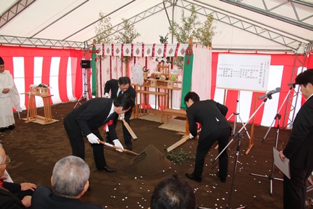 新庁舎の建設安全祈願祭りで盛り砂にカマをいれる3人のスーツの男性の写真