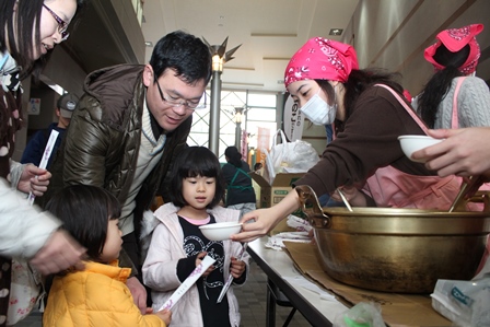 エプロンをつけた学生たちが、来場者たちにおこげ料理をふるまっている写真