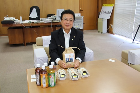 市長がお米のパッケージを手に笑顔でカメラのほうを向いている写真