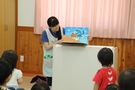 保育士の女性が動物の紙芝居を読み上げている写真