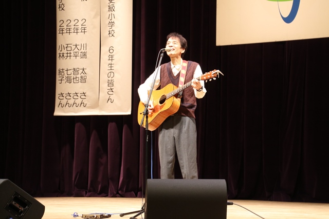 ギターを手に持った山本さんがマイクの前で歌っている写真