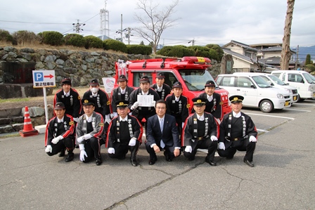 消防車の前にしゃがんで記念撮影をする市長と団員らの写真