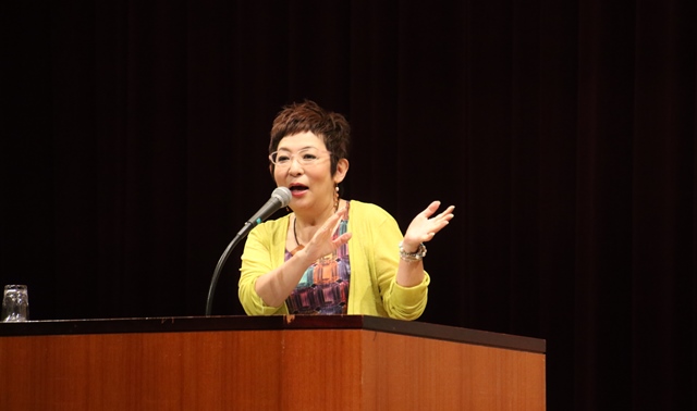 演壇で身振り手振りを交えて話す講師の菊田さんの写真