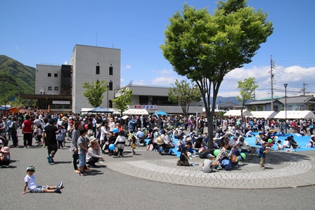 青空の下、来場者たちが広場に集まっている写真