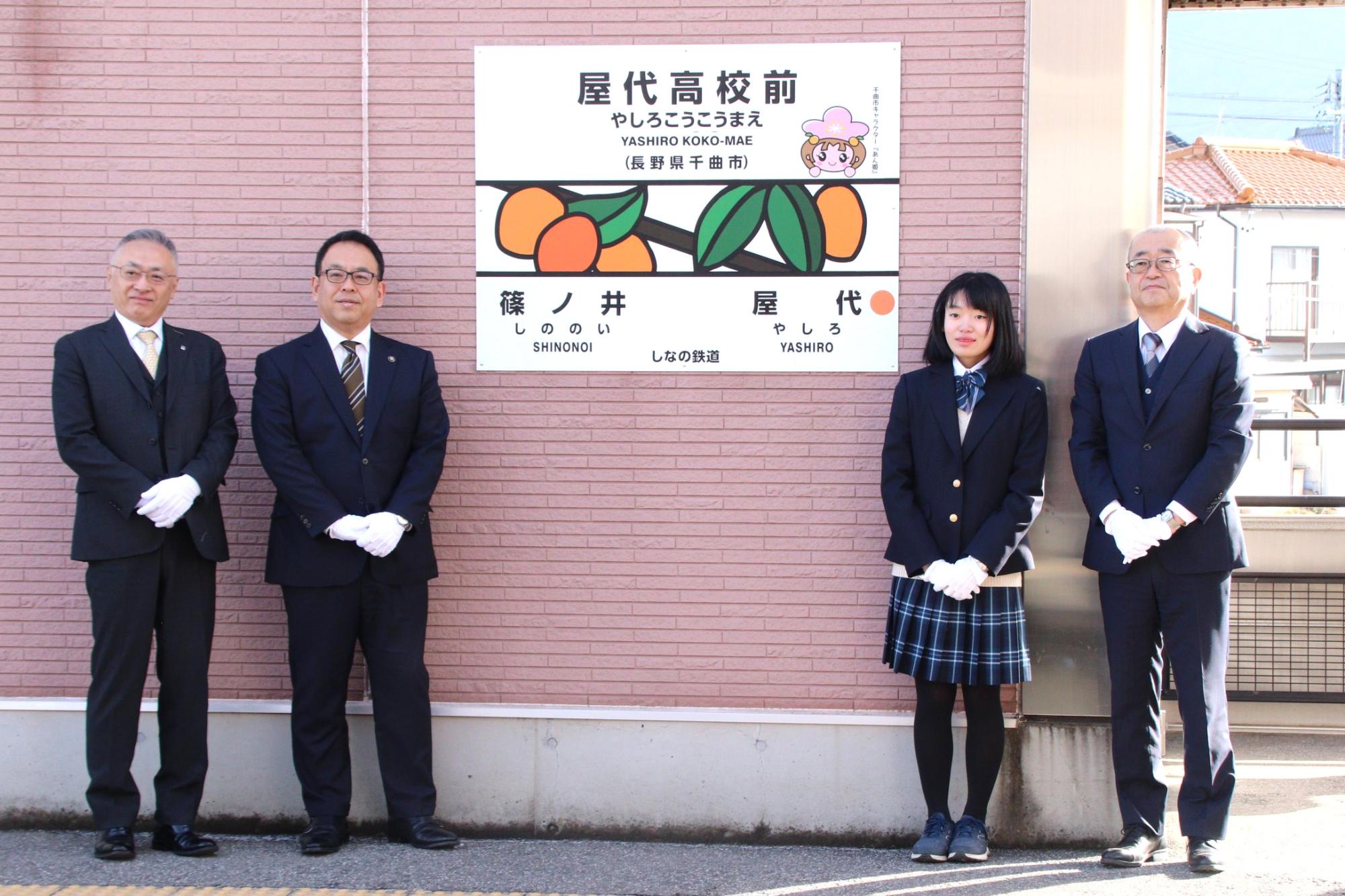 上りホーム駅名標を背景とした記念写真（左からしなの鉄道株式会社土屋智則代表取締役社長、小川修一市長、屋代高等学校1学年相澤綾香さん、同校馬場正一校長）