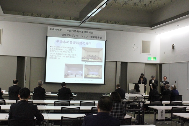 会議室の中でスクリーンを使い公開プレゼンテーションの様子の写真