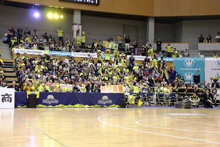 体育館の応援席でバスケットボールの試合を応援している観客の写真