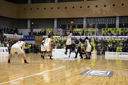 バスケットボールの試合中、ゴールへ向けてロングシュートをしている選手の写真
