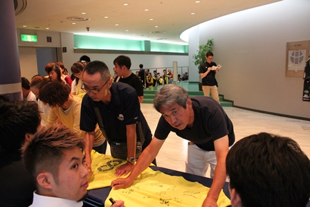 サイン会で黄色いTシャツにサインを入れている写真
