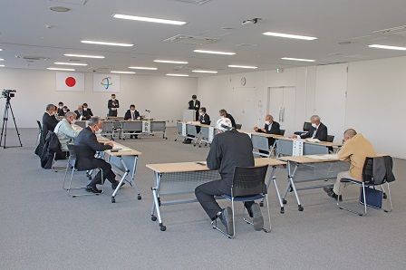 広い会議室内で机を向かい合わせて会議を行う議員たちの写真