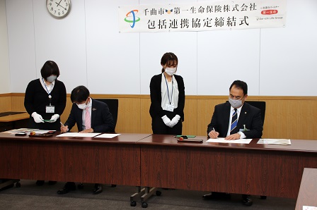 机に向かい合い、協定書に署名をしている市長と社長の写真