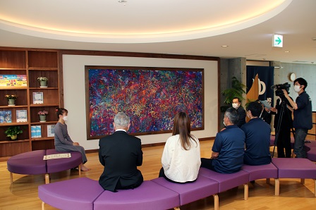 壁に設置された大きな絵画をソファに座りながら眺めている人たちの写真