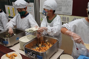 割烹着を着て給食の配膳を行う児童らの写真