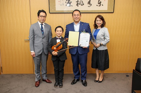 ヴァイオリンを持った小出くんと市長が記念撮影をしている写真