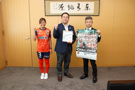 サイン色紙を手にガッツポーズをする市長と五嶋選手、町田社長の写真