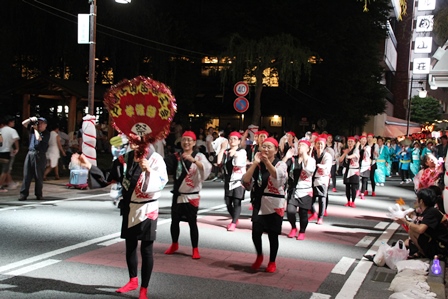 大きな飾りウチワを手に踊りを踊る参加者たちの写真