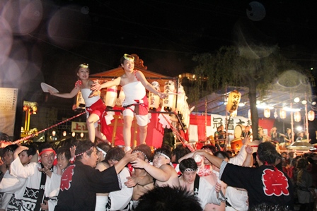 お神輿を担ぐ男性とお神輿の上で踊る女性の写真