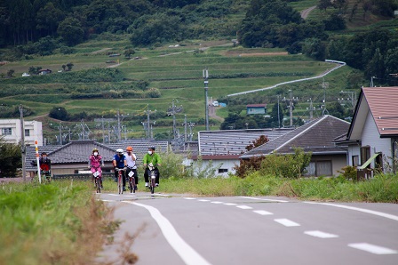自転車に乗った参加者たちがのどかな街並みを見渡すサイクリングロードを自転車で走る写真