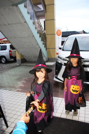 魔女の仮装をして商店街でお菓子をもらう女の子二人の写真