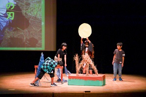 稲穂と満月の置物と一緒にステージ上で出し物を披露する子供たち写真