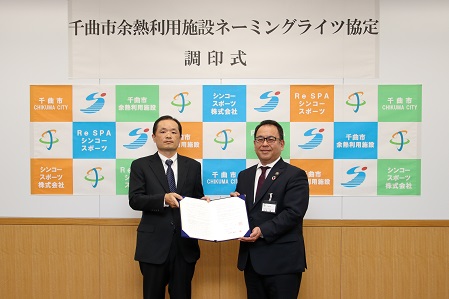 シンコースポーツ株式会社の石崎代表取締役と小川市長が協定書を手に持ち記念撮影