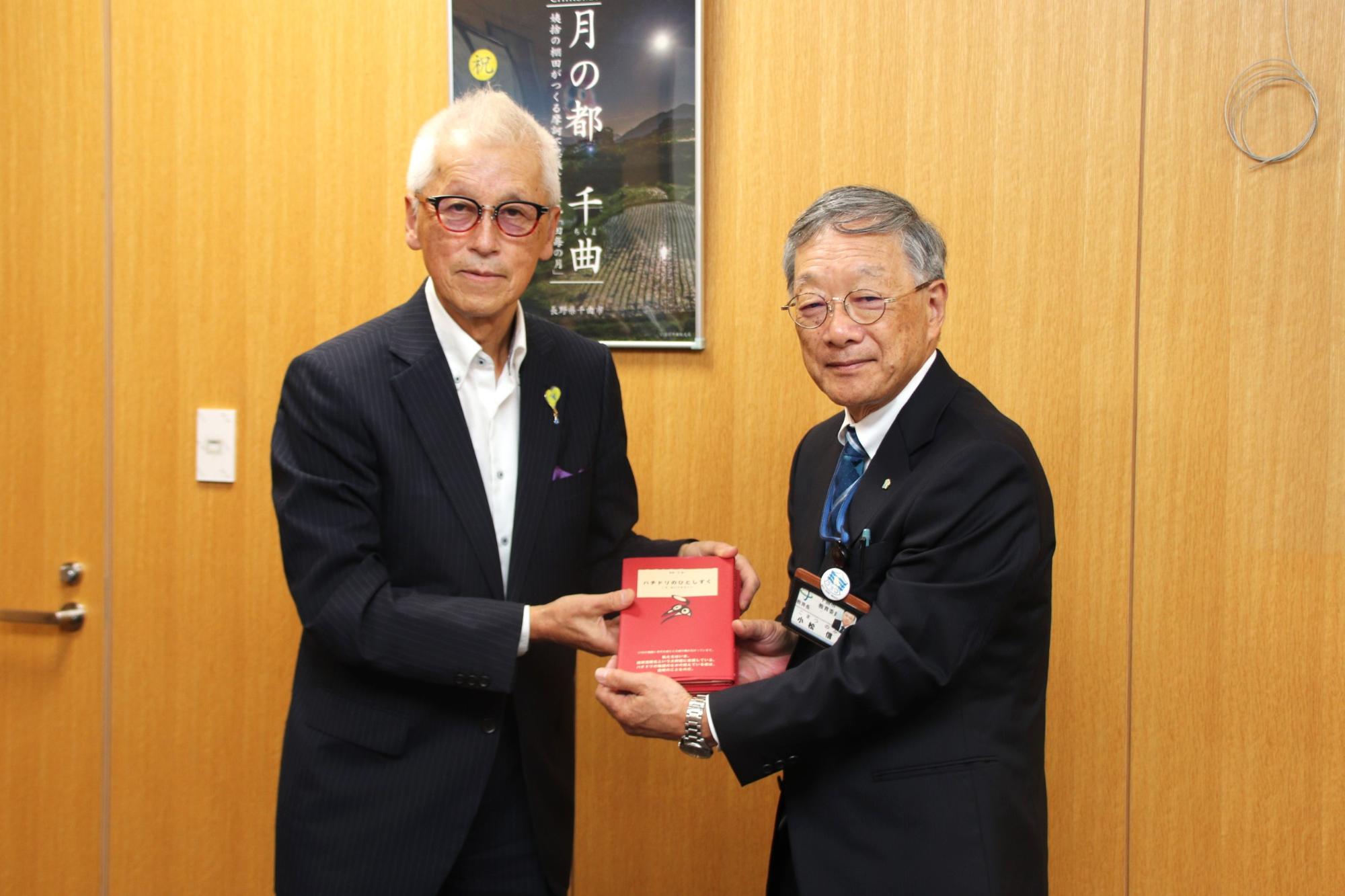 ハチドリのひとしずくの本を持って並ぶ小出会長（左）と小松教育長（右）