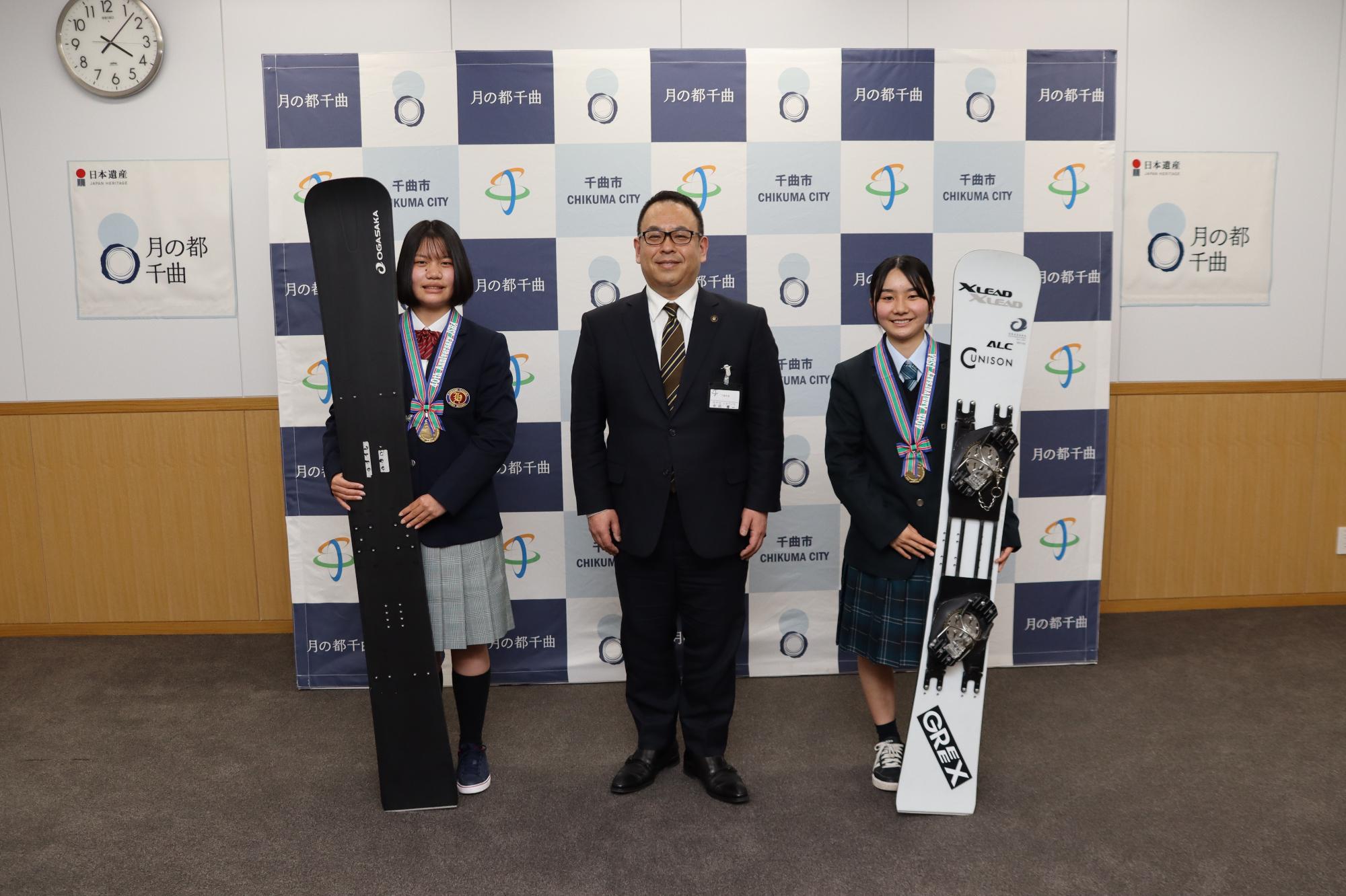 森下さん(左)と宮尾さん（右）がスノーボードとメダルをもって、小川市長（中央）と記念撮影