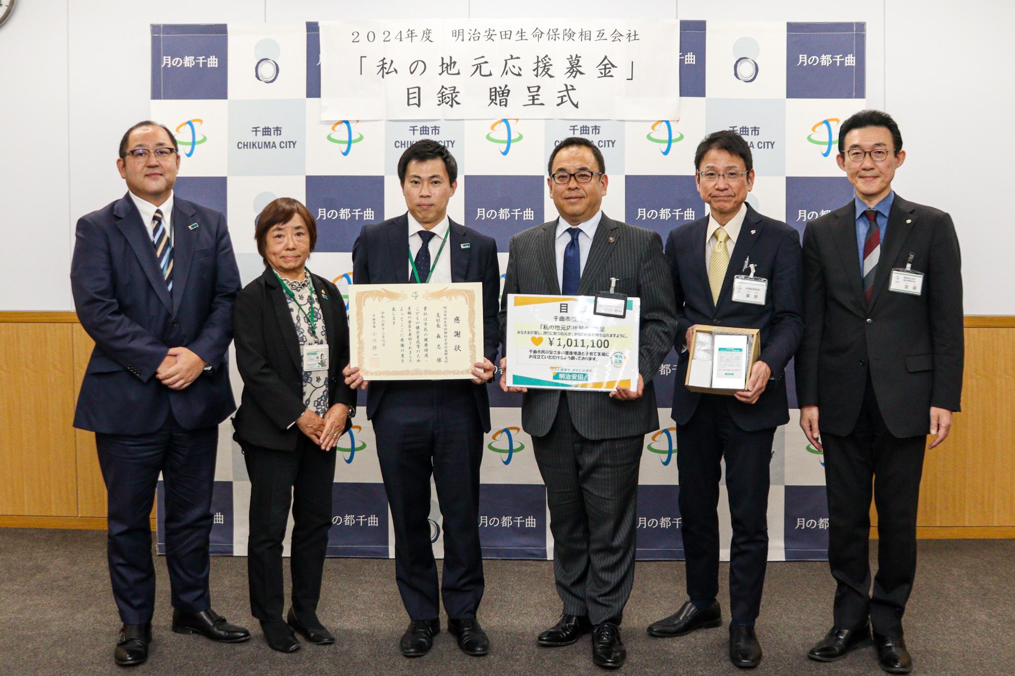 明治安田生命保険相互会社の担当者と市の関係者が賞状と目録を持って記念撮影