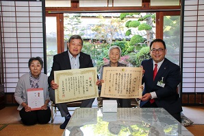 障子のある和室で田嶋さんとご家族が表彰状を手に持ち並んで記念撮影をしている写真